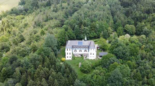 Luftaufnahme eines weißen Herrenhauses inmitten eines dicht bewaldeten Waldes.