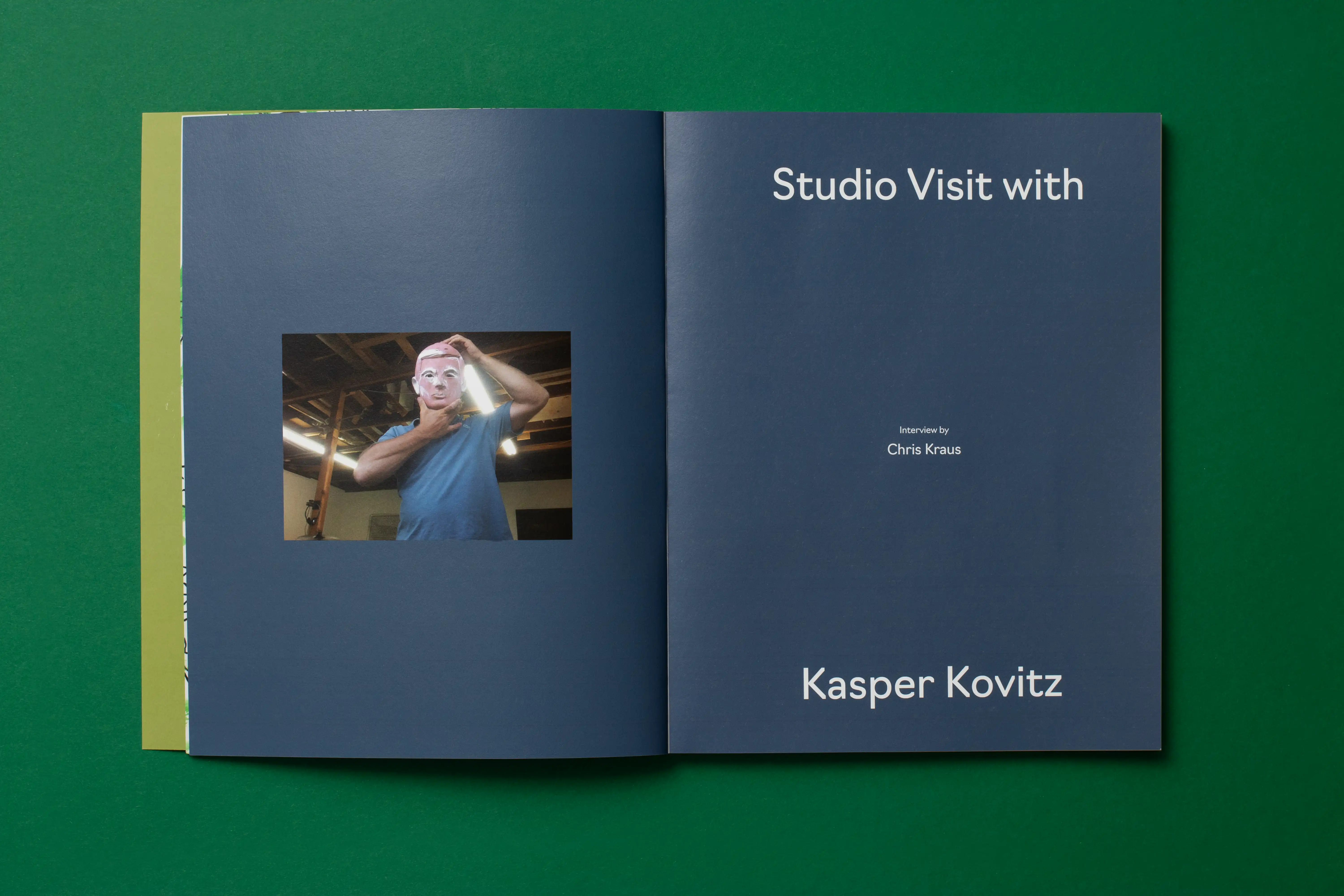 Open magazine on green surface; left page shows a person wearing a mask in a workshop; right page shows Studio Visit with Kasper Kovitz.